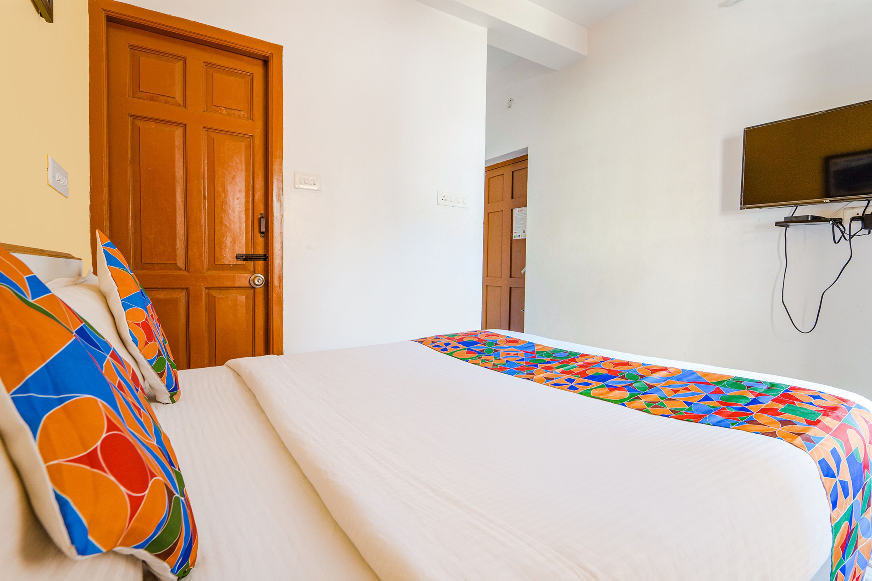 A hotel room with a bed, a wooden door, and a television mounted on the wall.