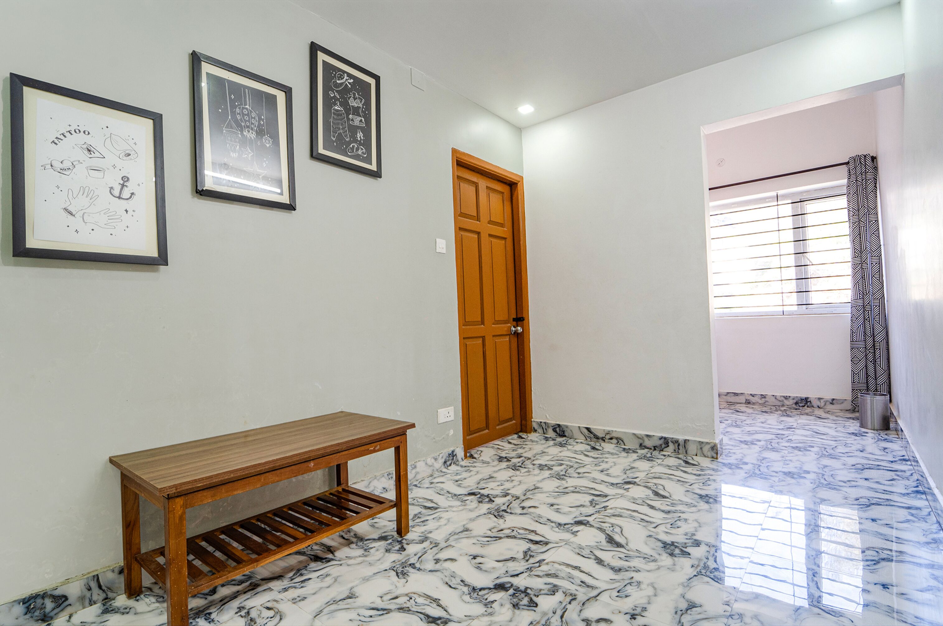 Un pasillo con un banco de madera, obras de arte enmarcadas en la pared, una puerta de madera y piso de mármol.