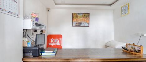 A reception desk with a computer, a calendar, a painting, and a clock on the wall.