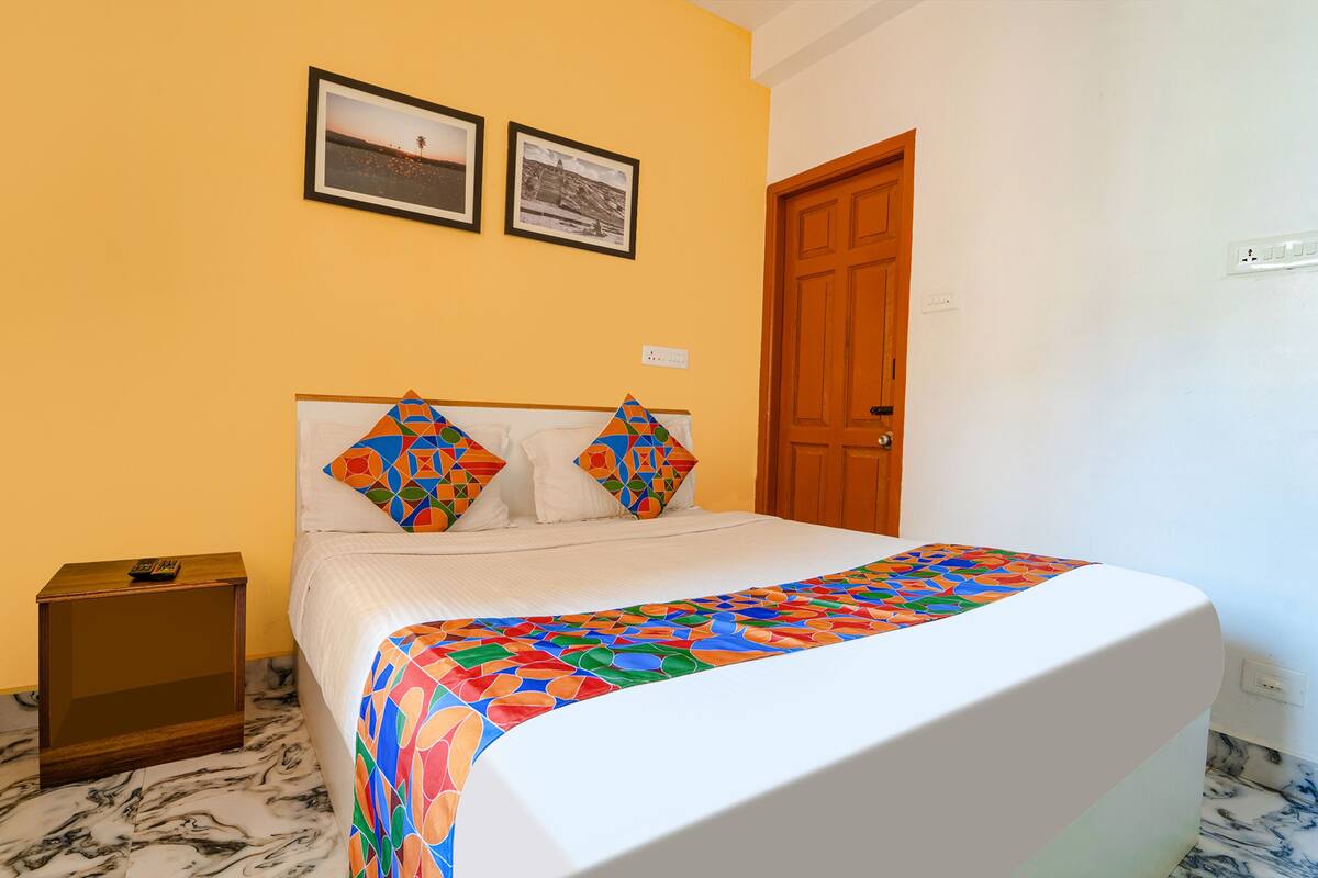 A bedroom with a bed, a nightstand, a wooden door, and two framed pictures on the wall.
