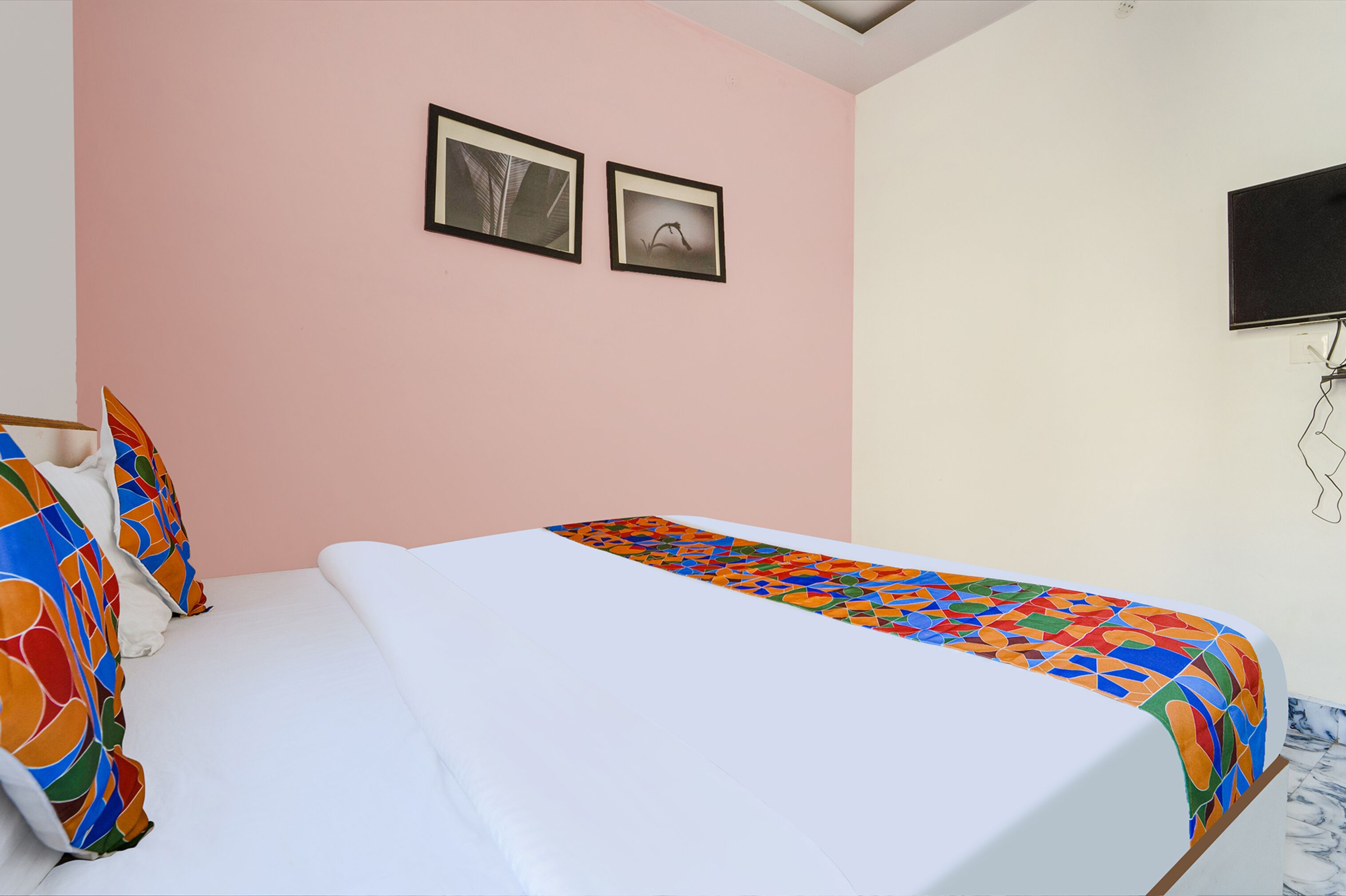 Un dormitorio con una cama, almohadas, una manta colorida y dos cuadros en la pared.