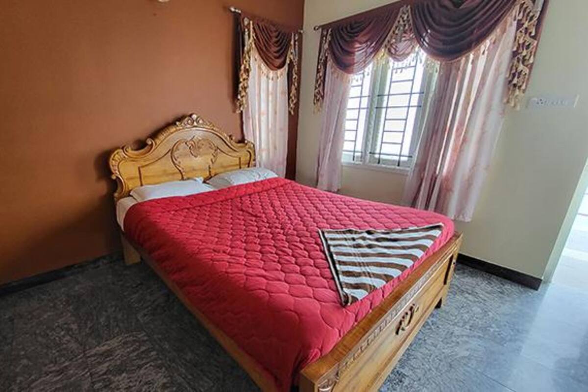 Ein Einzelbett mit Holz-Kopfteil, einer roten Steude und einem gestreiften Kopfkissen in einem Zimmer mit Marmorboden und einem fenster mit Vorhängen.