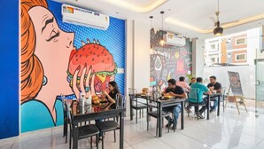 A restaurant with a vibrant mural on the wall, tables and chairs arranged for dining, and ceiling fans. - Fabhotel Aashiyana (Indore)