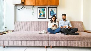 A pink sofa with two people sitting on it, one holding a phone and the other holding a cup. There are two framed artworks on the wall behind them. - Fabhotel Aashiyana (Indore)