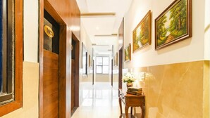 A hotel corridor with wooden doors, numbered room signs, framed landscape paintings, and a marble floor. - Fabhotel Aashiyana (Indore)