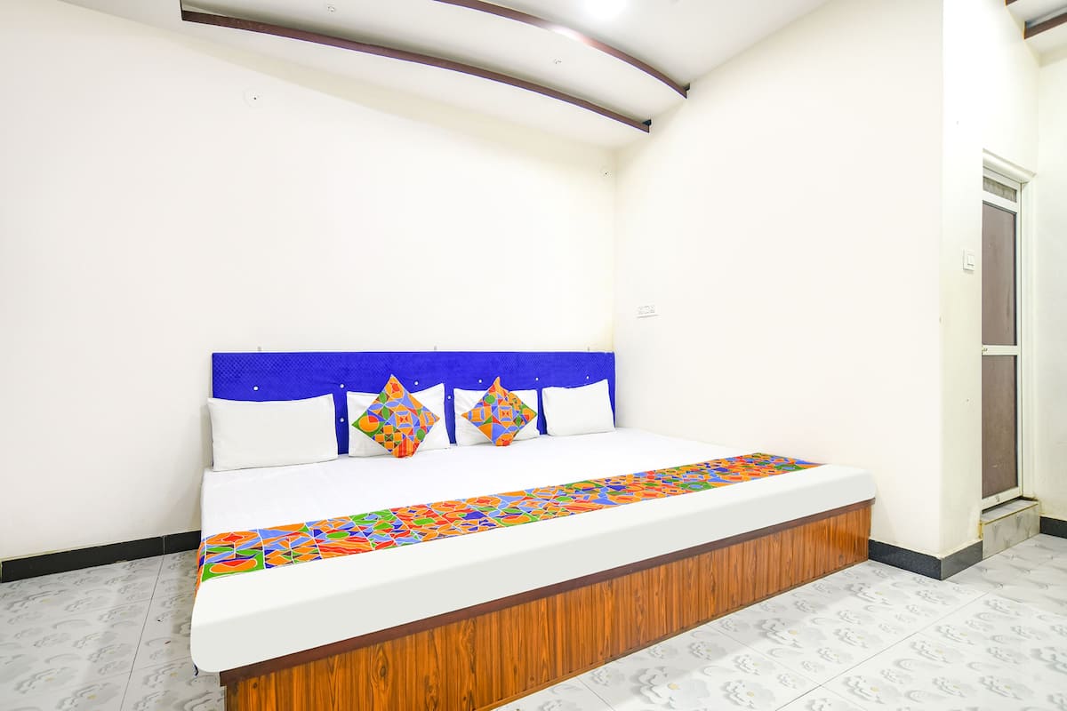 Un dormitorio con una cama individual, paredes blancas, cabecera de madera y colcha colorida.