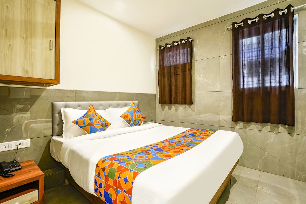 A hotel room with a bed, a nightstand, a telephone, and a window with curtains.