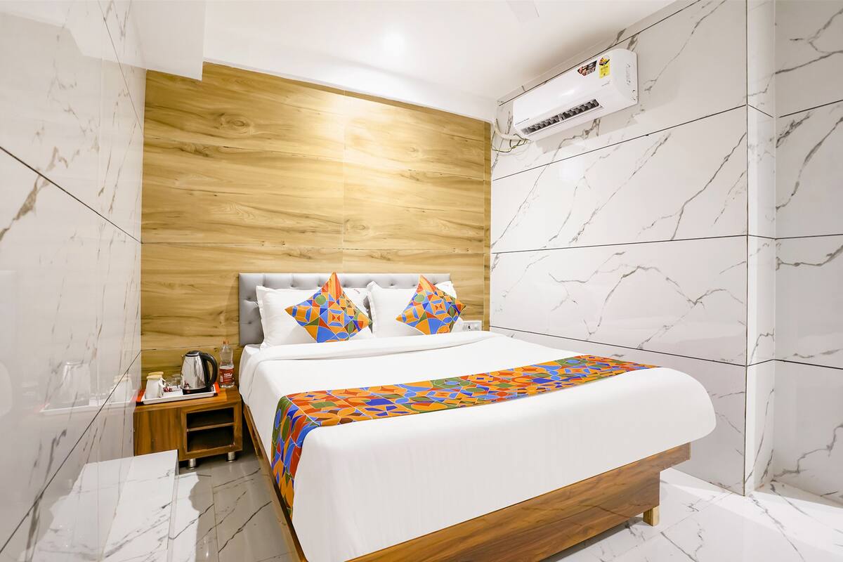 A hotel room with a bed, wooden panel wall, marble flooring, and an air conditioning unit.