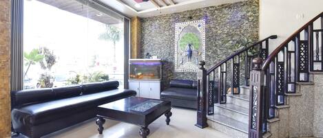 Un hall con un sofá de cuero negro, un acuario y una escalera con barandillas ornamentadas.