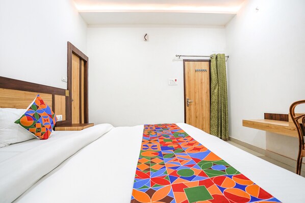 A hotel room with a bed, a wooden headboard, a bedside table, a chair, and a window with curtains.
