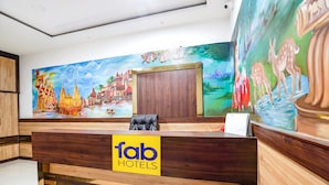A hotel reception desk with a wooden finish, a 'fab hotels' sign, and a mural depicting a traditional scene with buildings and animals. - FabHotel Vairagi Inn - Nr. Bhojuveer Chauraha, Shivpur (Varanasi)