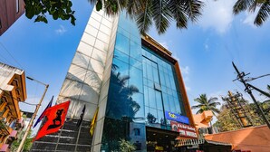 A modern hotel with a glass facade, a prominent red flag, and a sign for JNV Hotels. - FabHotel JVH (Bengaluru)