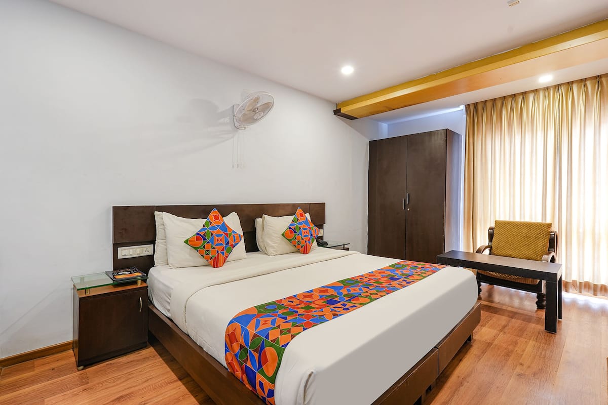 A neatly arranged hotel room with a large bed, a bedside table, a wardrobe, and a chair by the window.
