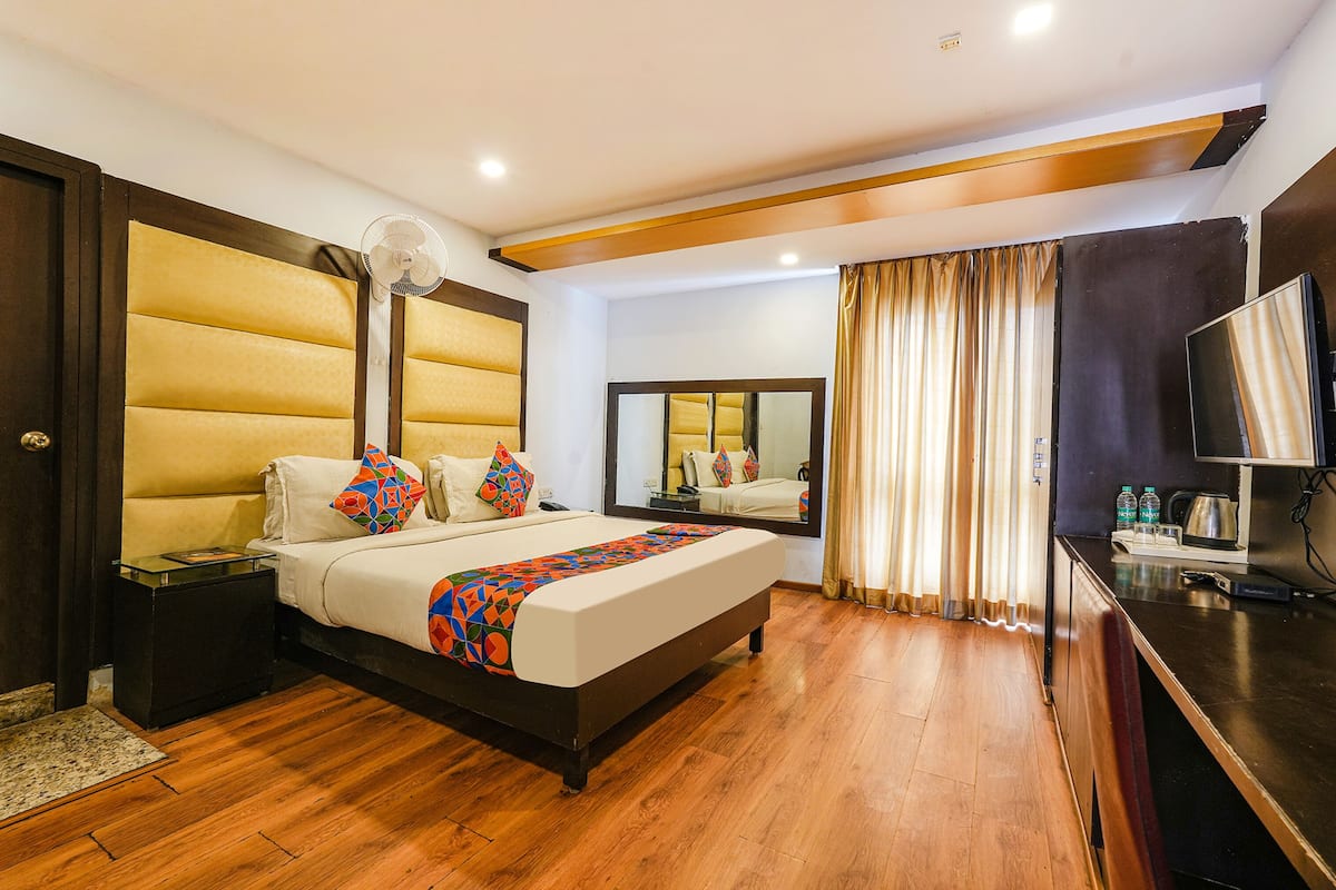 A hotel room with a bed, bedside table, mirror, curtains, and a TV.