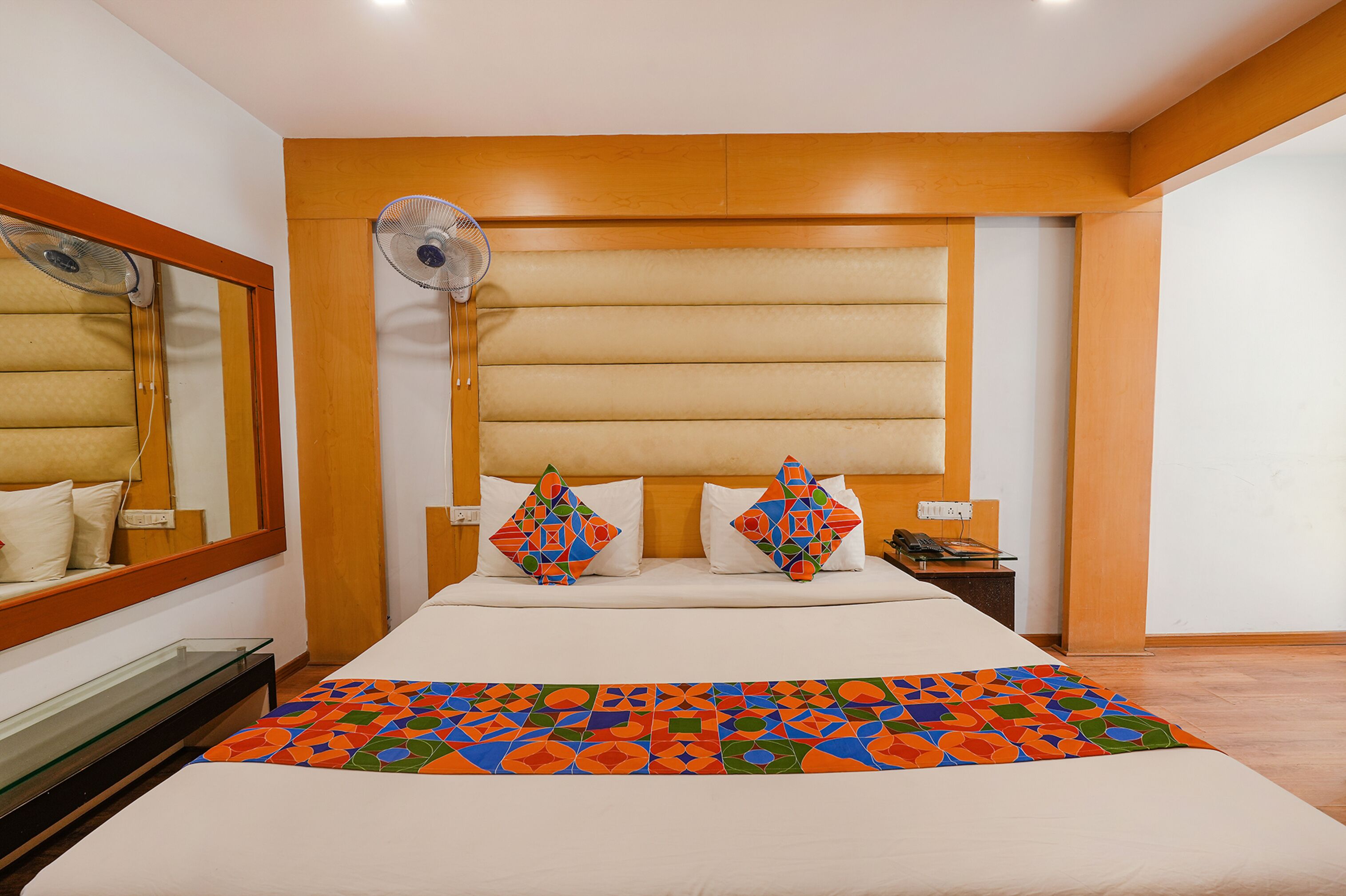 A hotel room with a large bed, a bedside table, a mirror, and a wall-mounted fan.
