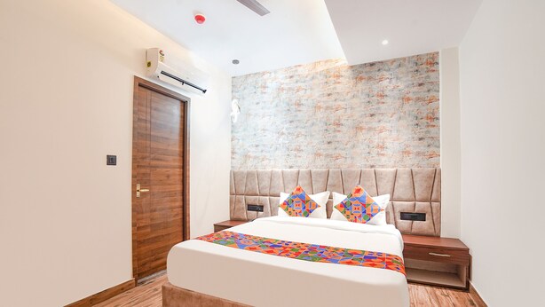 A modern bedroom with a wooden floor, a large bed with a colorful bedspread, a headboard with a geometric pattern, and a wall-mounted air conditioning unit. - Fabhotel The Comfort Inn (Kanpur)