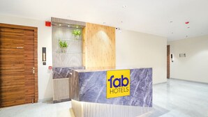 A reception desk with a marble top and a wooden panel design, a potted plant, and a sign reading "fab hotels". - Fabhotel The Comfort Inn (Kanpur)