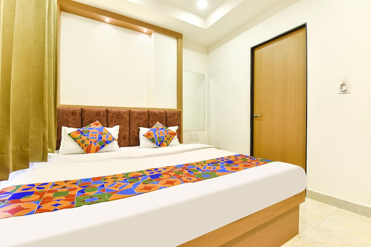 A hotel room with a large bed, a wooden headboard, a colorful bed runner, and a door to the right.