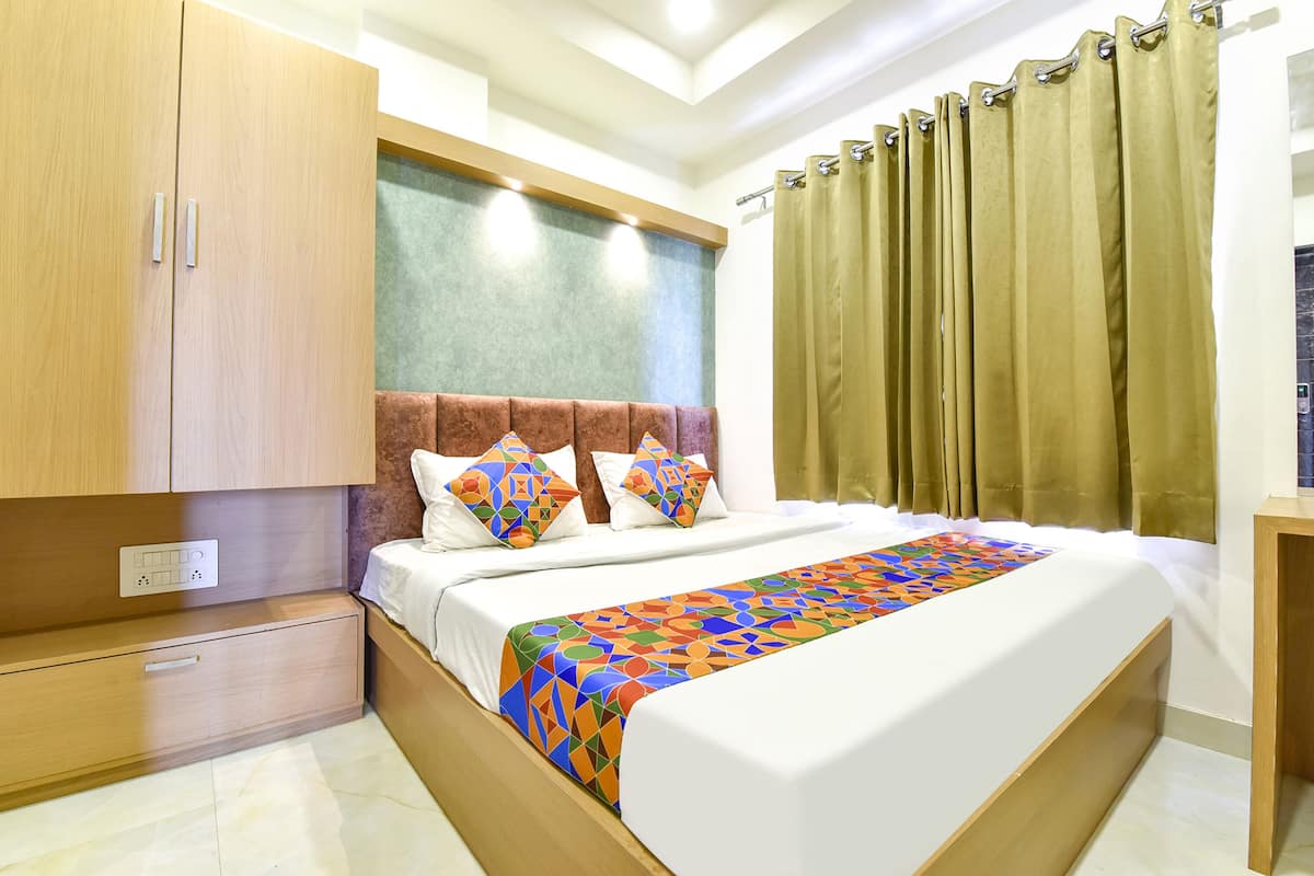 A hotel room with a large bed, a wooden wardrobe, and a window with curtains.