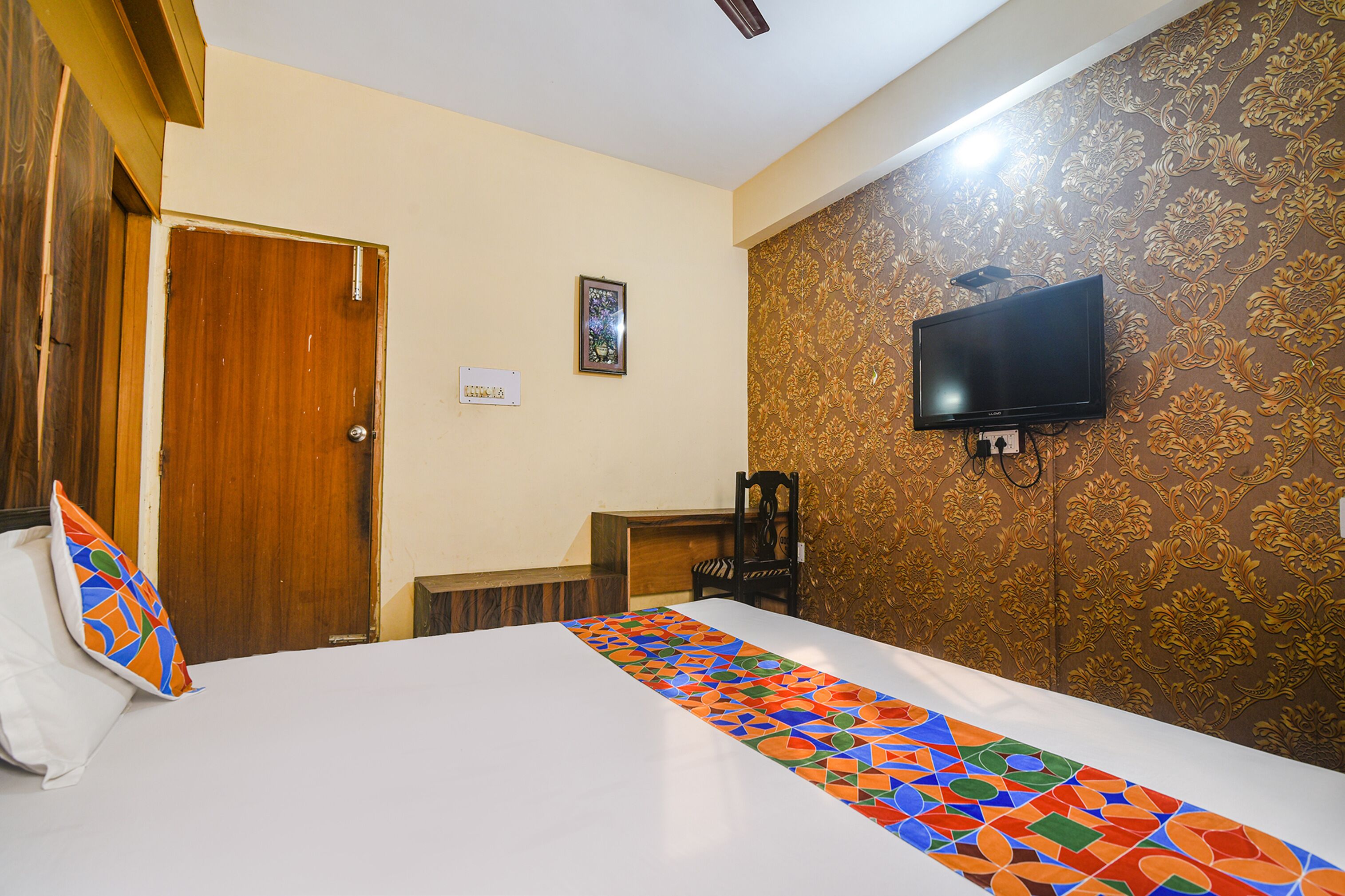 A hotel room with a bed, a television mounted on the wall, a wooden door, and a patterned wallpaper.