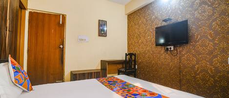 A hotel room with a bed, a television mounted on the wall, a wooden door, and a patterned wallpaper.