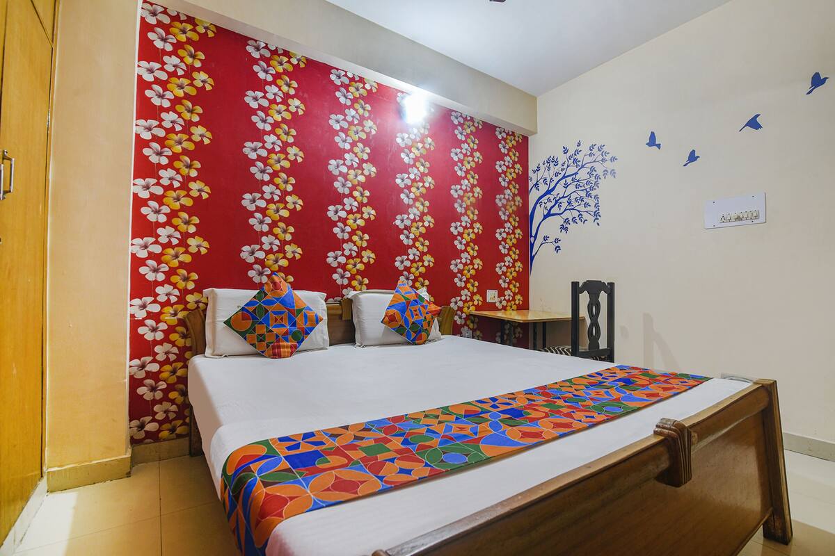 A hotel room with a bed, a wooden wardrobe, a red floral wall, and a wall decoration of birds.