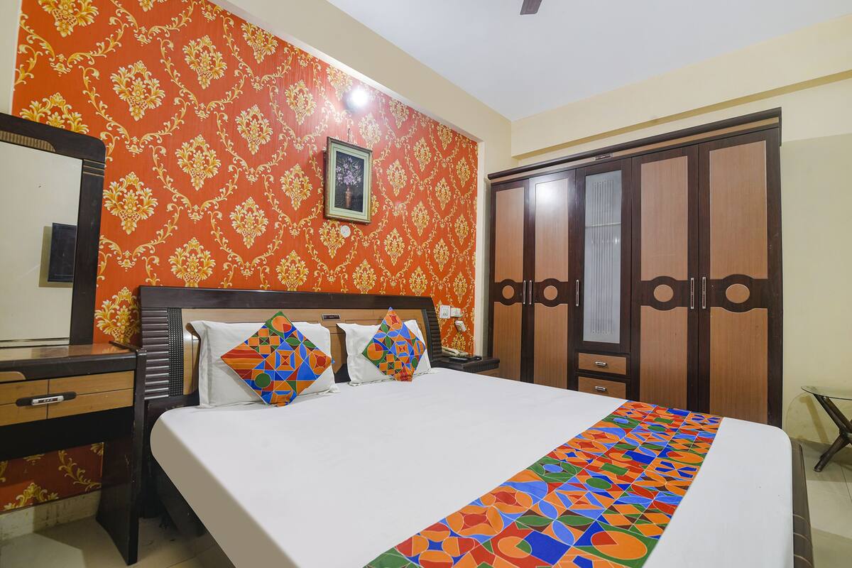 A hotel room with a bed, a wooden wardrobe, a desk, and a mirror.