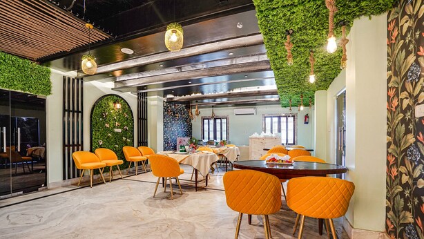 A dining area with a round table, orange chairs, and a green wall with hanging lights. - Fabhotel Prime Stay Inn I (Varanasi)