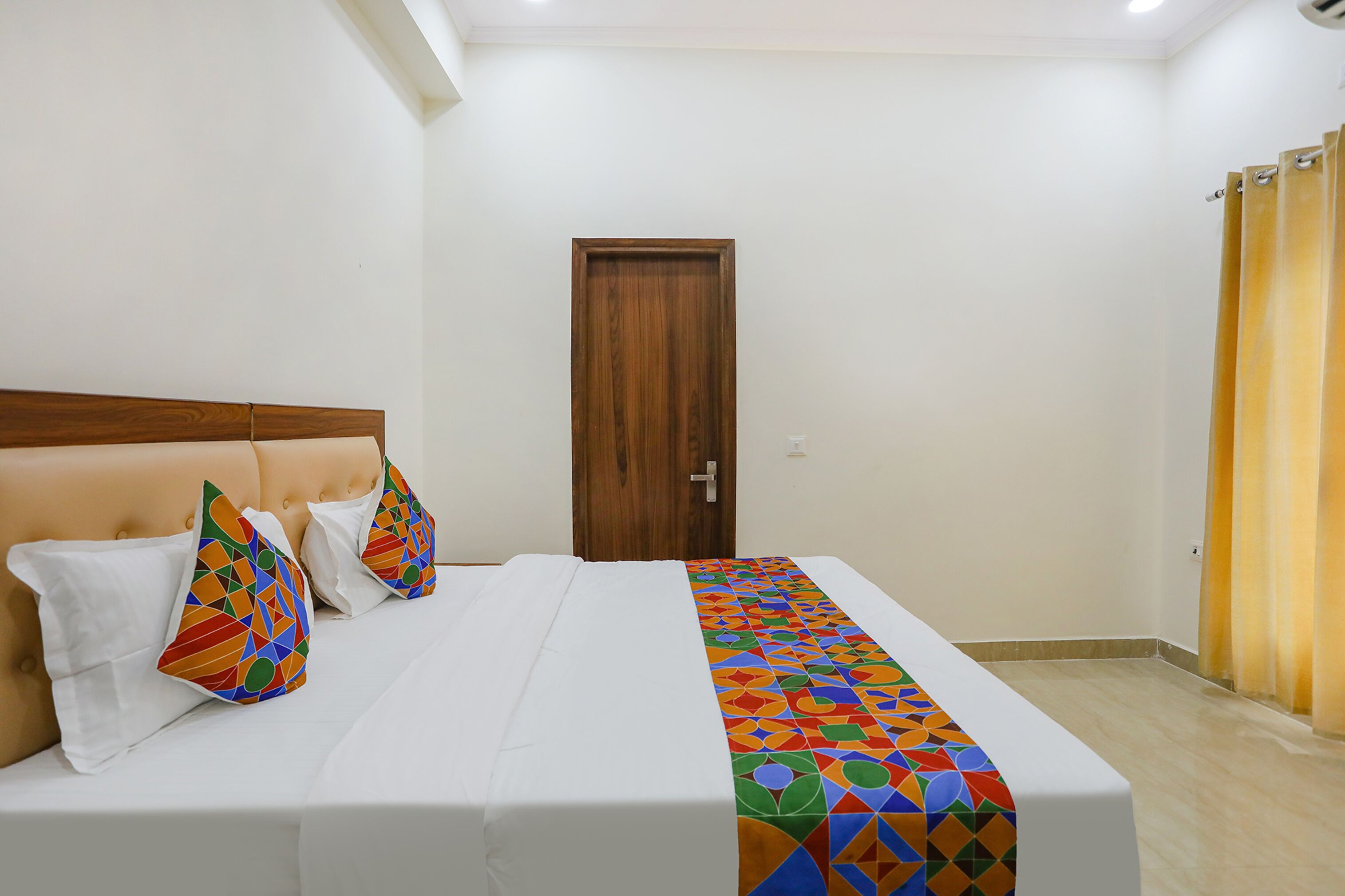 A neatly made bed with a patterned bedspread, two pillows with geometric designs, and a wooden headboard.