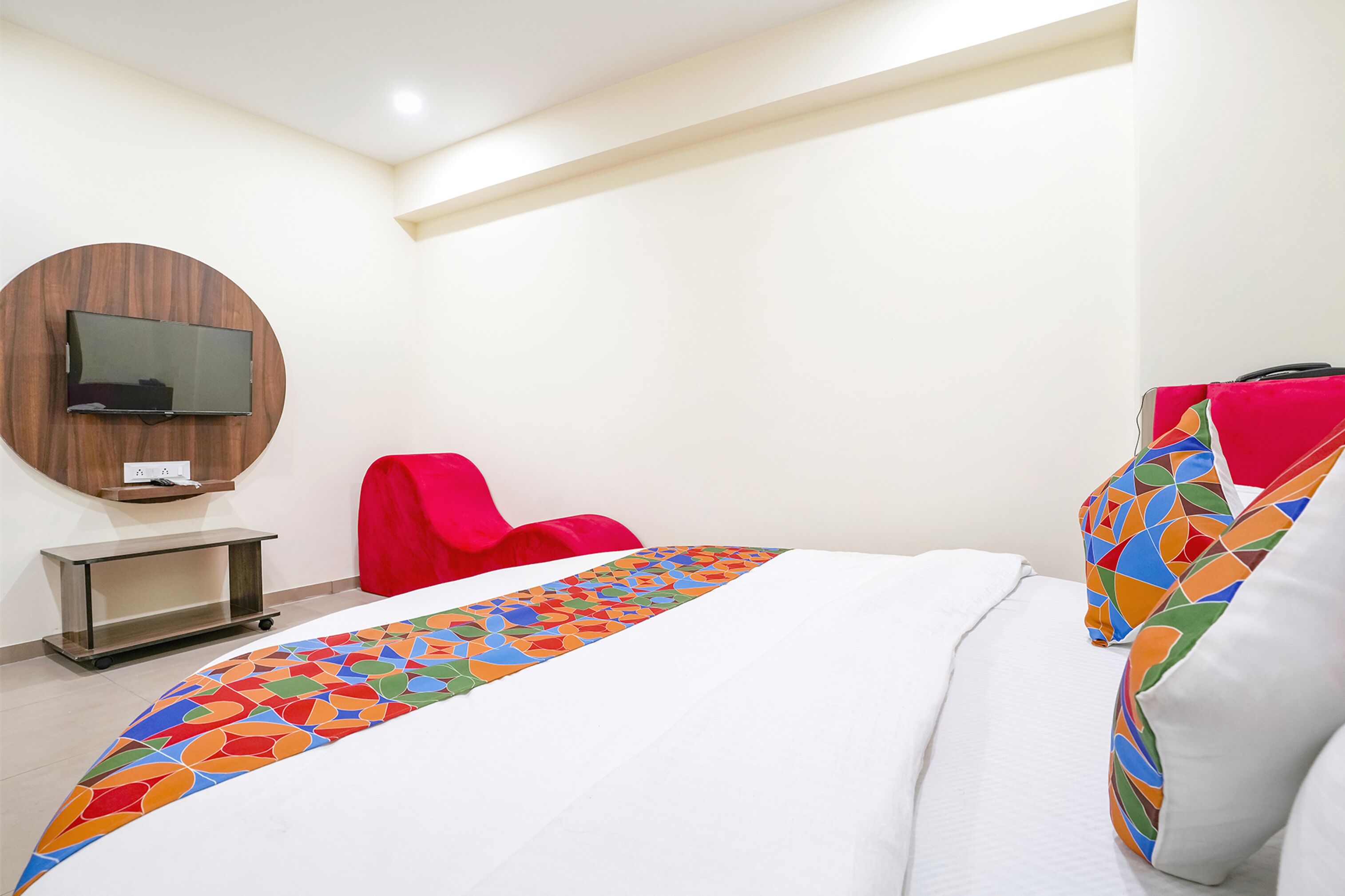 A hotel room with a bed, a TV mounted on the wall, a red chair, and a small table.