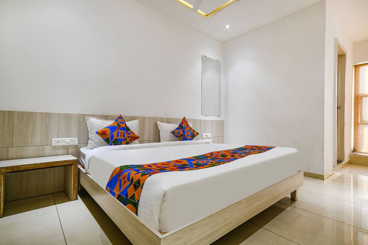 Habitación de hotel moderna con una cama grande, una mesita de noche, un espejo y una ventana con persianas.