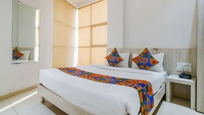 Habitación de hotel ordenada con una cama grande, una mesita de noche, un espejo y una ventana con persianas.