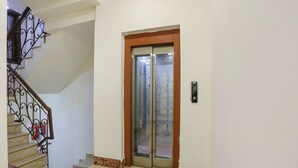 A staircase with a metal railing, a fire extinguisher, and a door with a glass panel. - Fabhotel East Patel Nagar (New Delhi)