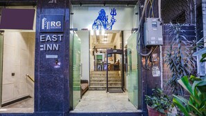 The entrance to East Inn with a sign for RG Buildingwell Group, a staircase leading inside, and potted plants outside. - Fabhotel East Patel Nagar (New Delhi)