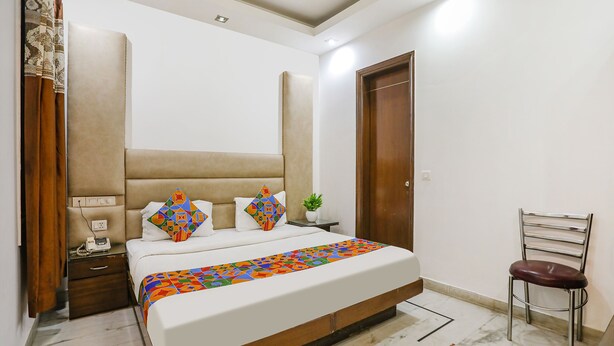A bedroom with a large bed, a wooden headboard, a nightstand with a lamp, a chair, and a potted plant. - Fabhotel East Patel Nagar (New Delhi)