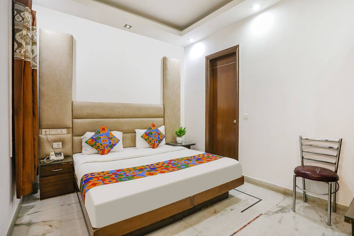 A bedroom with a large bed, a wooden headboard, a nightstand with a lamp, a chair, and a potted plant.