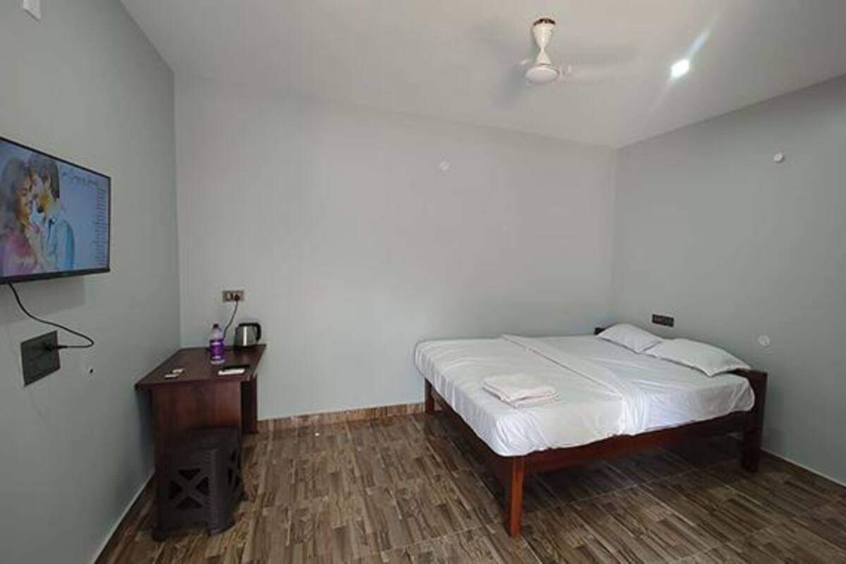 Quarto com cama, mesa de cabeceira, televisão e ventoinha no teto.