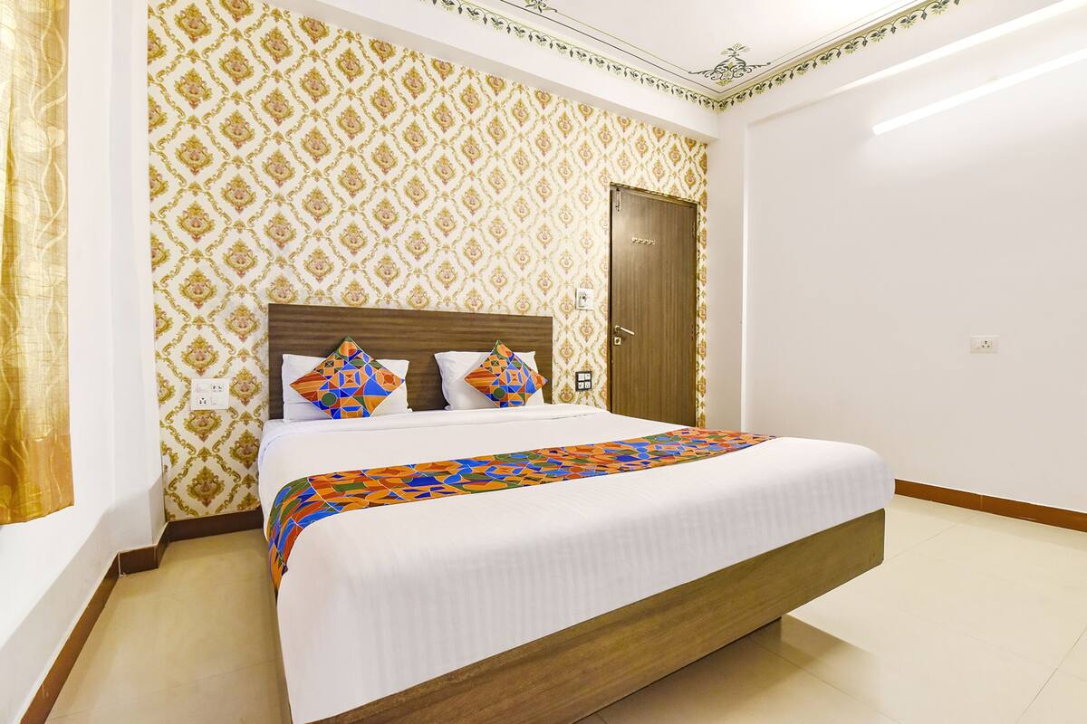 A hotel room with a large bed, patterned wallpaper, a wooden headboard, and a door.
