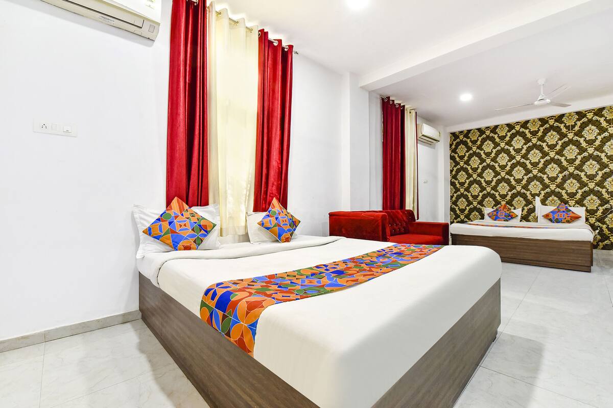 A hotel room with a large bed, a red sofa, a small table, and a patterned wallpaper.