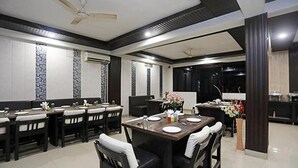 A modern dining area with a long table, black chairs, and a decorative vase. - Fabhotel Taj Castle (Agra)