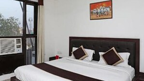 A hotel room with a large bed, a ceiling fan, a window with a view, and a painting on the wall. - Fabhotel Taj Castle (Agra)