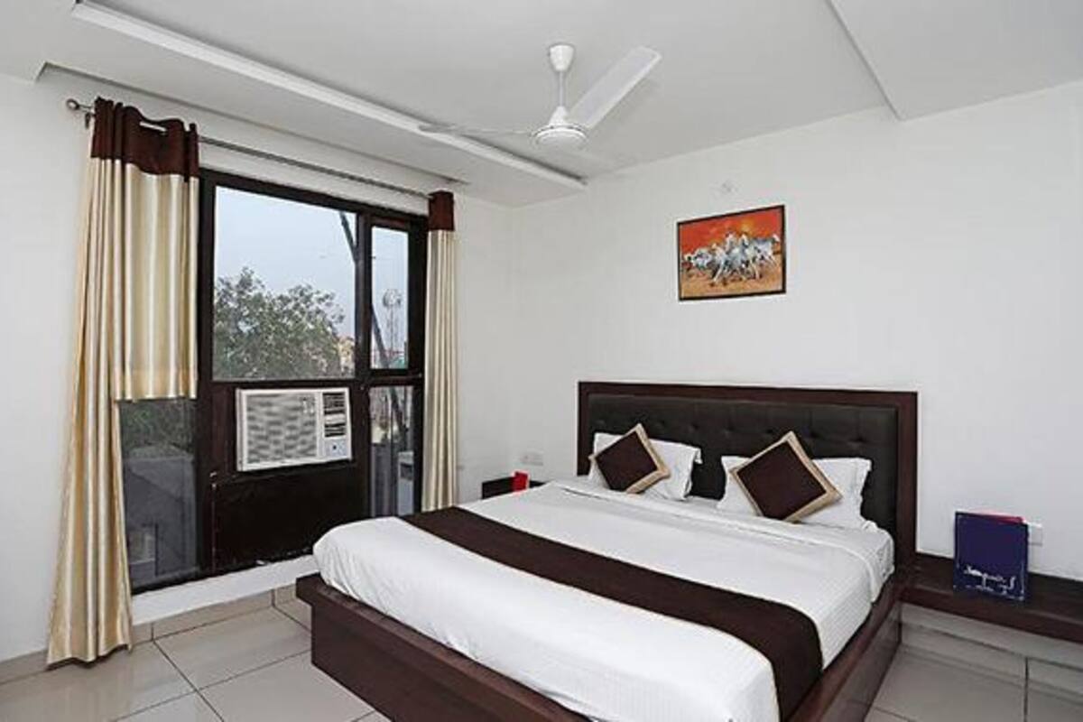 A hotel room with a large bed, a ceiling fan, a window with curtains, and a painting on the wall.