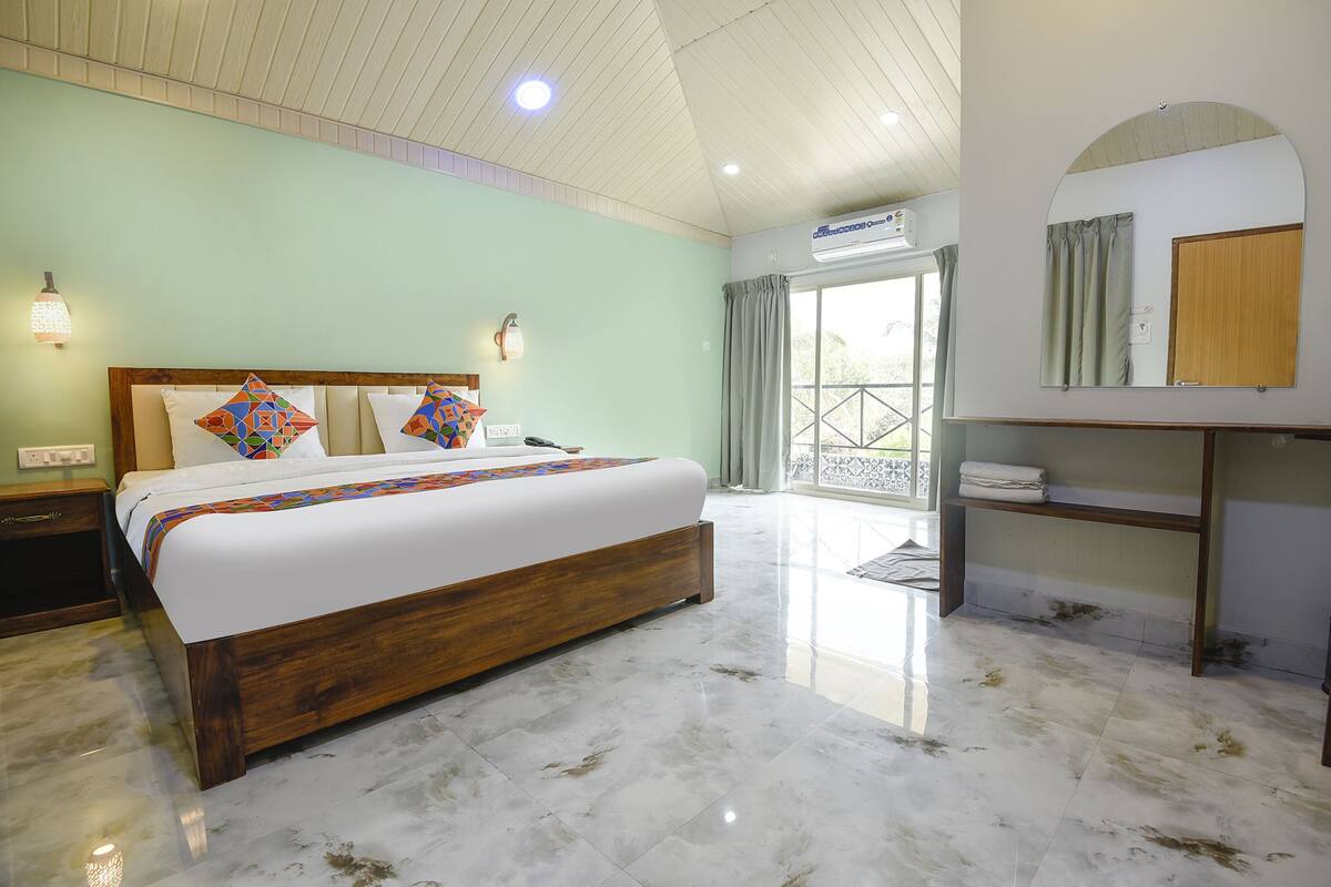 A bedroom with a large bed, a wooden headboard, a nightstand, a wall-mounted shelf, and a window with curtains.