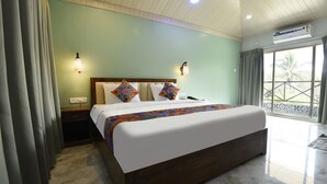 A hotel room with a large bed, two wall-mounted lights, a nightstand, a window with curtains, and an air conditioning unit. - Fabhotel Prime 4D'S Coast Resort (Vagator)