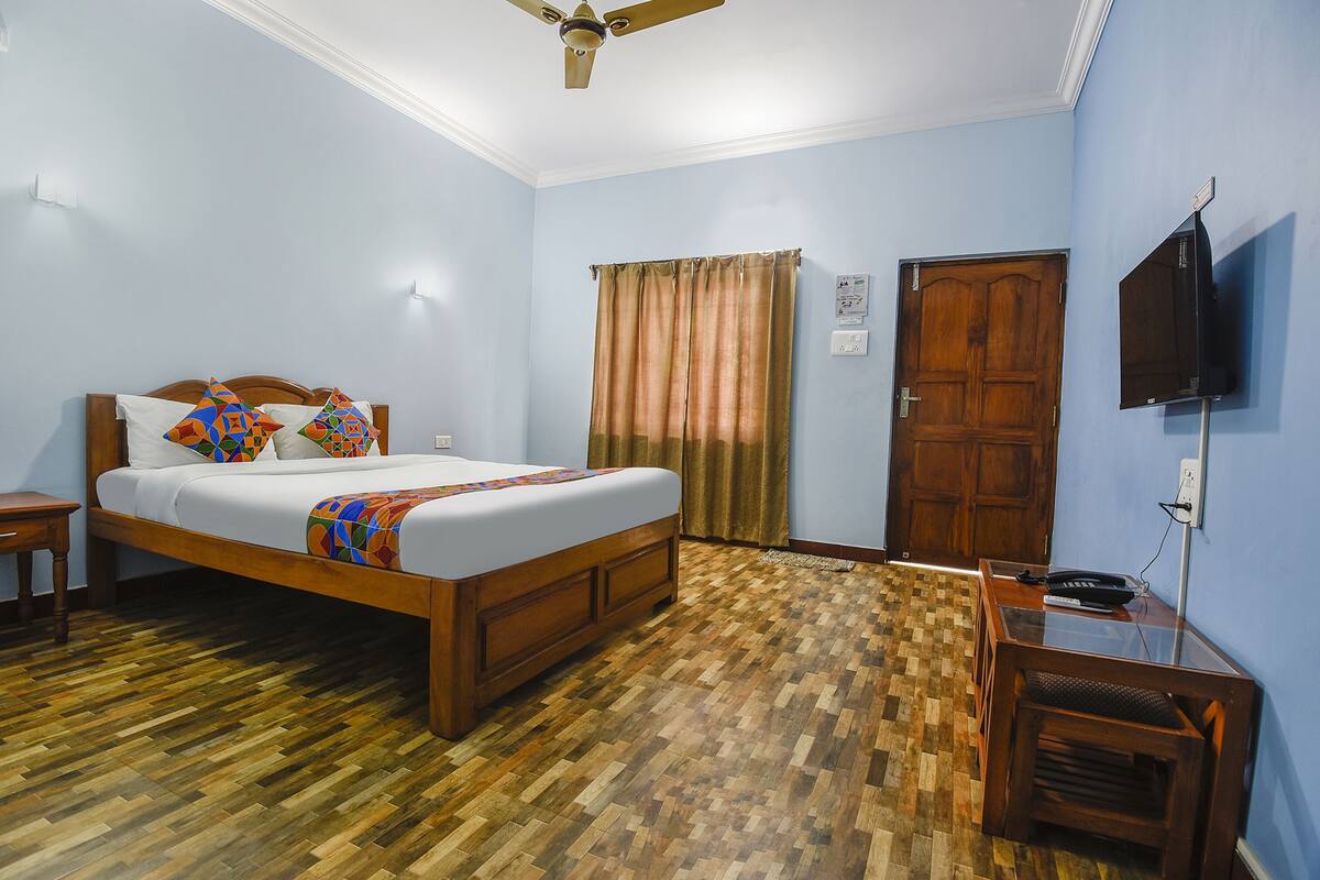 A bedroom with a wooden bed, a ceiling fan, a wooden door, and a TV mounted on the wall.
