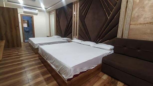 A hotel room with two beds, a dark brown sofa, wooden flooring, and a large window with curtains. - Fabexpress Rudraksh Palace (Ujjain)