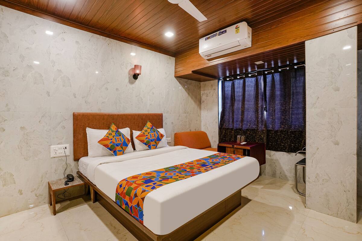 Una habitación de hotel con cama, mesita de noche, escritorio y ventana con cortinas.