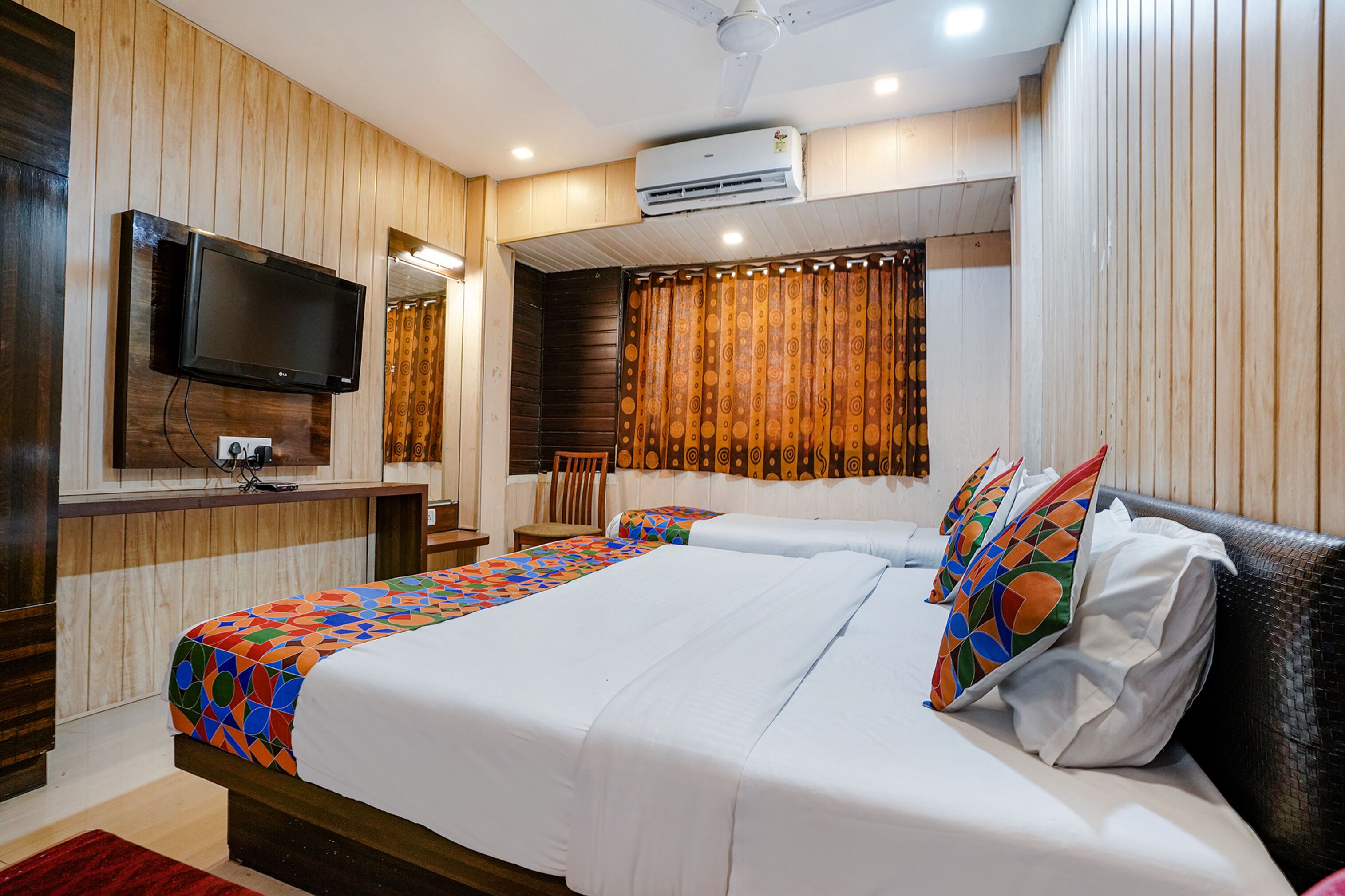 A hotel room with a bed, a TV, a chair, and a window with curtains.