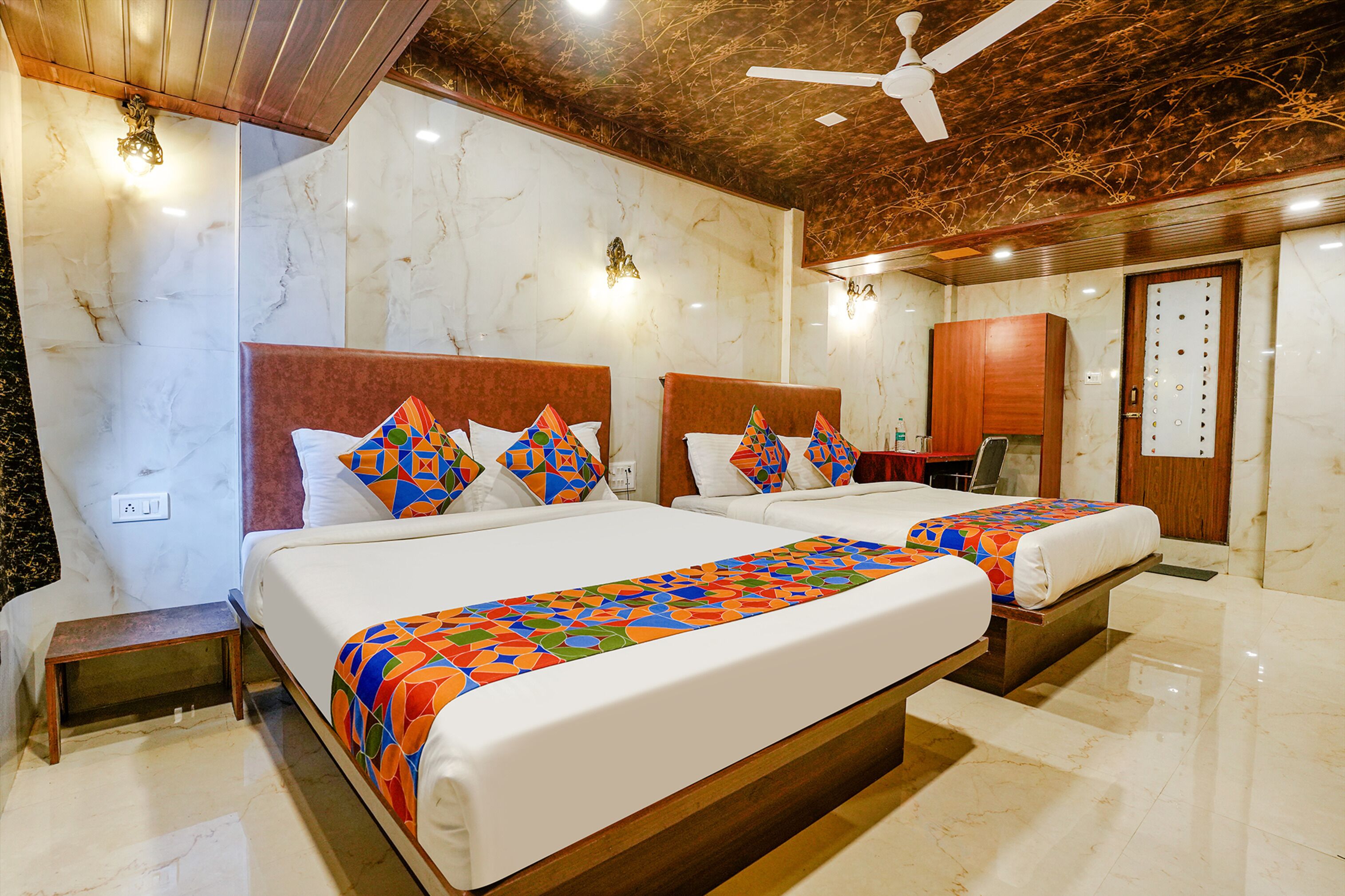 A hotel room with two beds, marble walls, wooden headboards, and a ceiling fan.