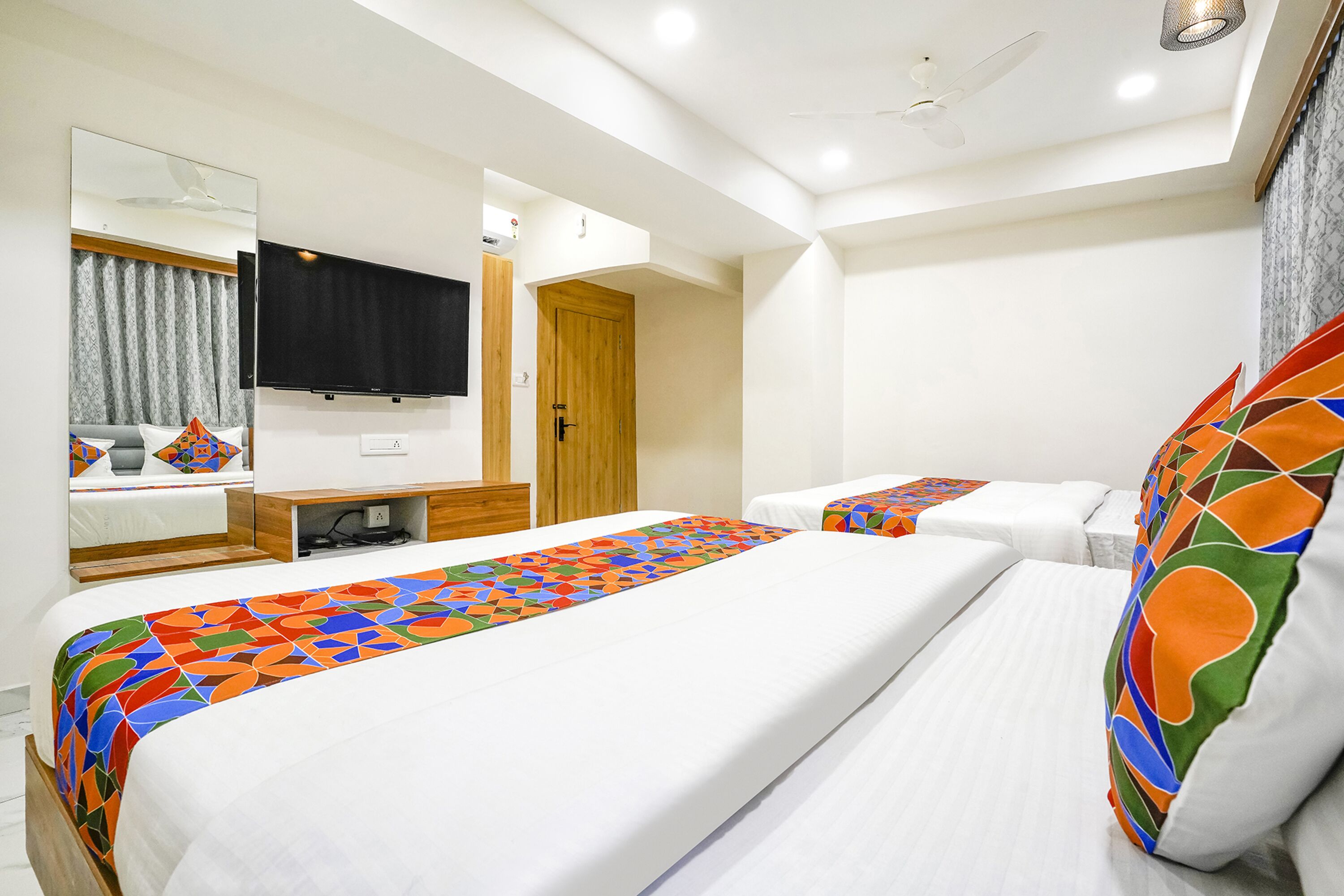 Habitación de hotel con dos camas, un televisor, una puerta de madera y un ventilador de techo.
